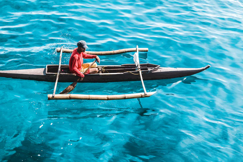 Fisherman paddling an outrigger bangka across clear blue water in Cebu